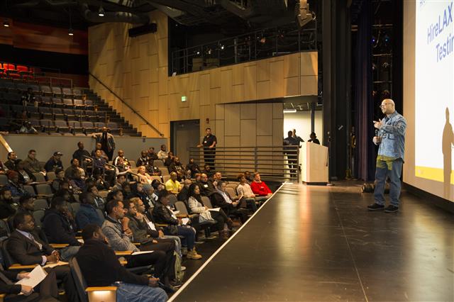 Man on stage giving an HireLAX testimonial at an orientation for the second class of the HireLAX program.